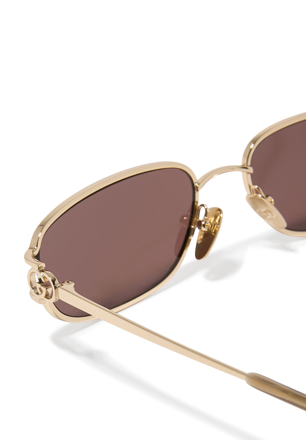 Close-up of gold-frame luxury sunglasses with brown lenses and interlocking G logo detail.