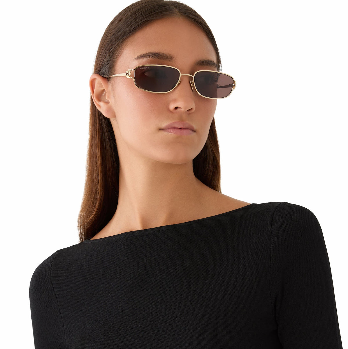 Woman wearing gold-framed Gucci luxury sunglasses with dark lenses and a black top.