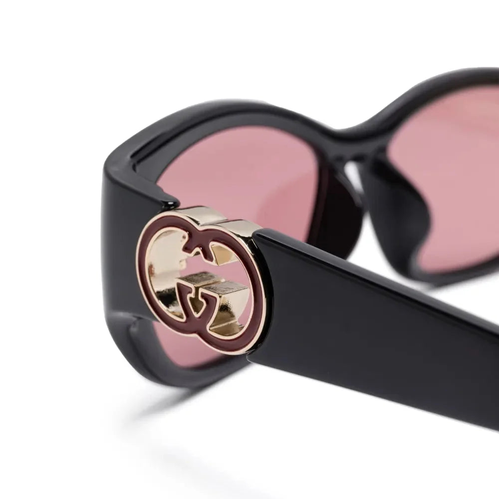 Close-up of luxury black sunglasses with pink lenses and gold designer logo detail.