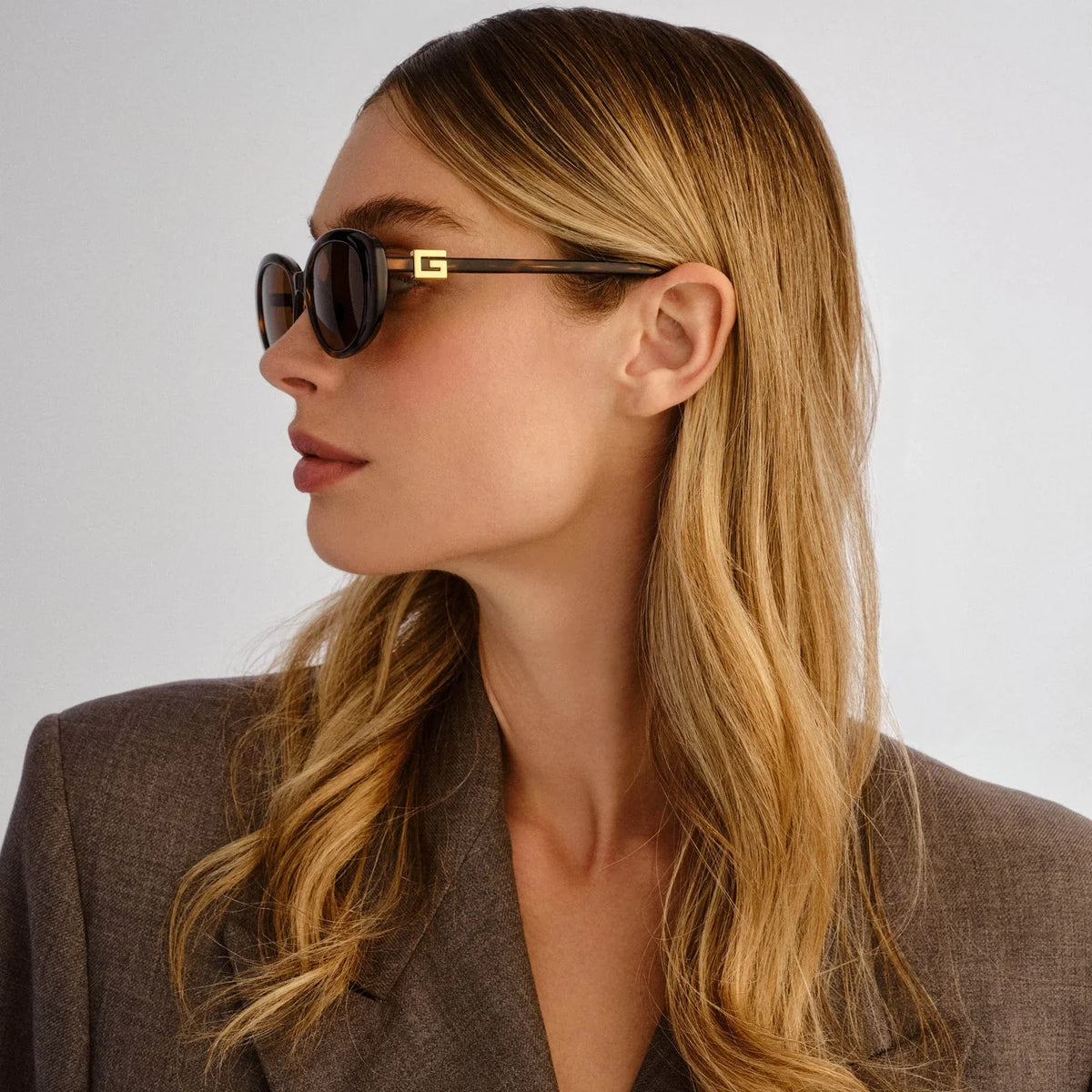 Side profile of a woman wearing luxury tortoiseshell sunglasses with gold accents.