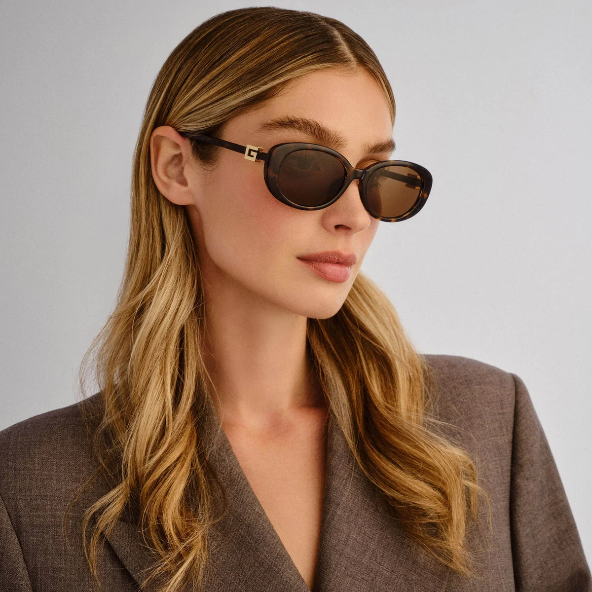 Woman wearing premium dark brown oval sunglasses and a grey blazer