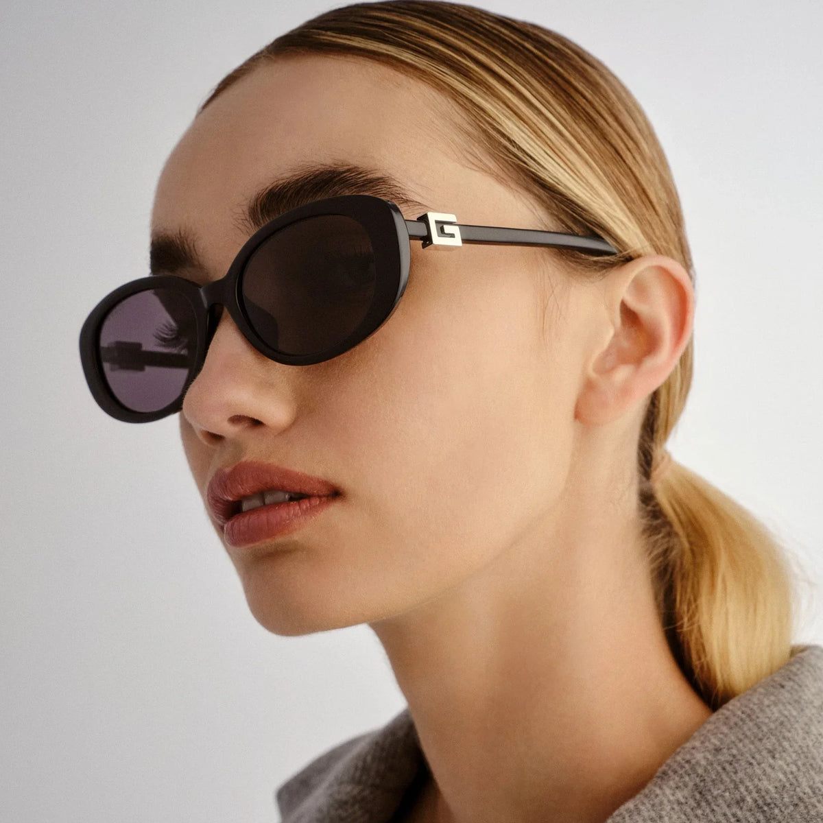 Woman wearing oversized black designer sunglasses with gold logo detail.